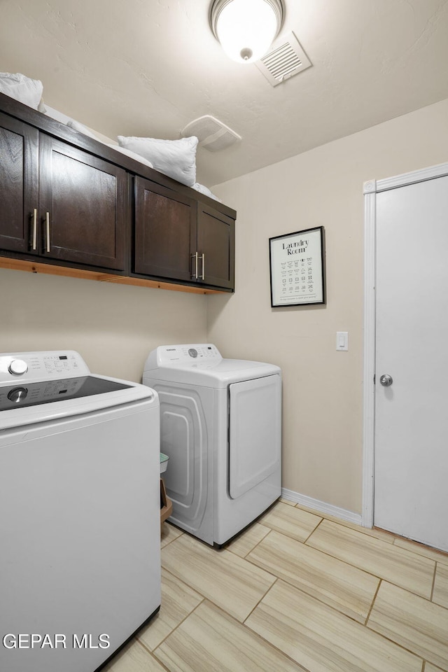clothes washing area with washer and dryer, visible vents, and cabinet space