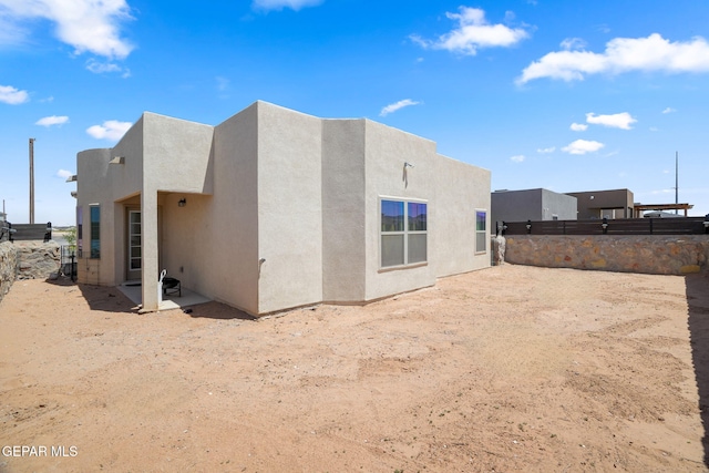 rear view of house with stucco siding and fence