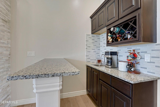kitchen with a sink, dark brown cabinets, tasteful backsplash, light wood finished floors, and a peninsula