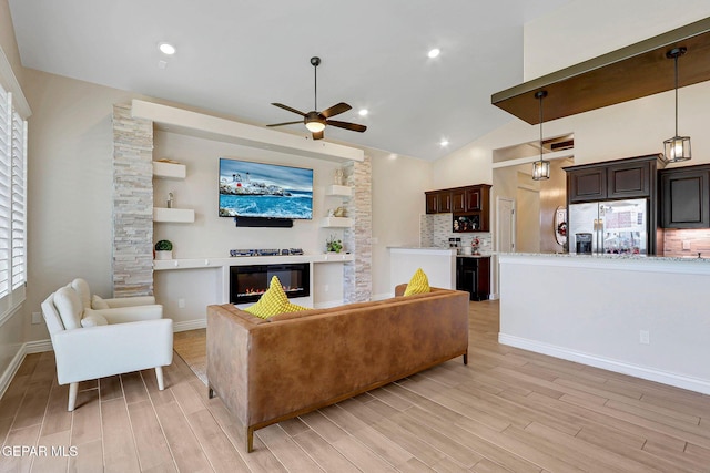 living room featuring a ceiling fan, light wood-style flooring, a glass covered fireplace, and high vaulted ceiling