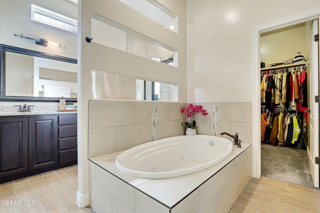 bathroom featuring wood finished floors, a tub with jets, a spacious closet, and vanity