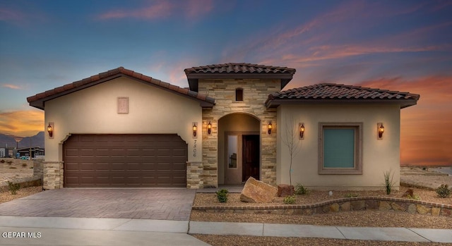 mediterranean / spanish house featuring stucco siding, a garage, a tiled roof, and driveway