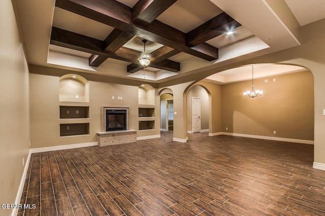 unfurnished living room with wood finished floors, coffered ceiling, baseboards, beamed ceiling, and arched walkways