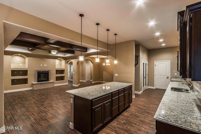 kitchen with a sink, dark brown cabinetry, arched walkways, dark wood-style floors, and baseboards