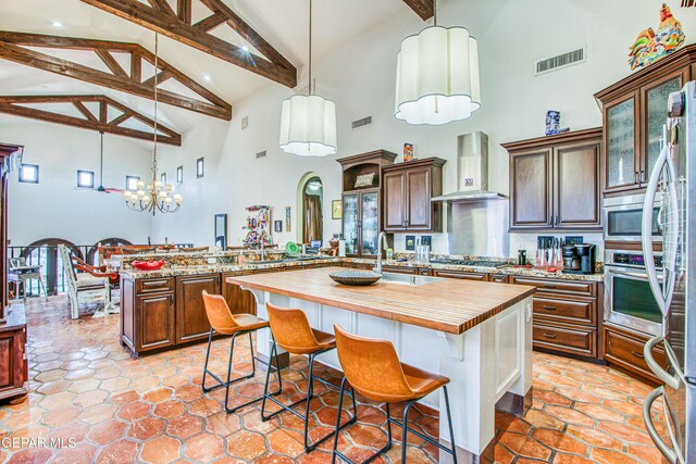kitchen with wood counters, wall chimney exhaust hood, appliances with stainless steel finishes, beamed ceiling, and high vaulted ceiling
