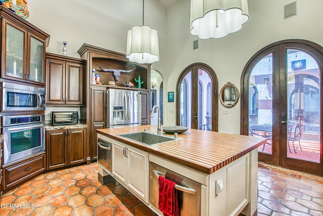 kitchen with french doors, appliances with stainless steel finishes, arched walkways, a sink, and a high ceiling