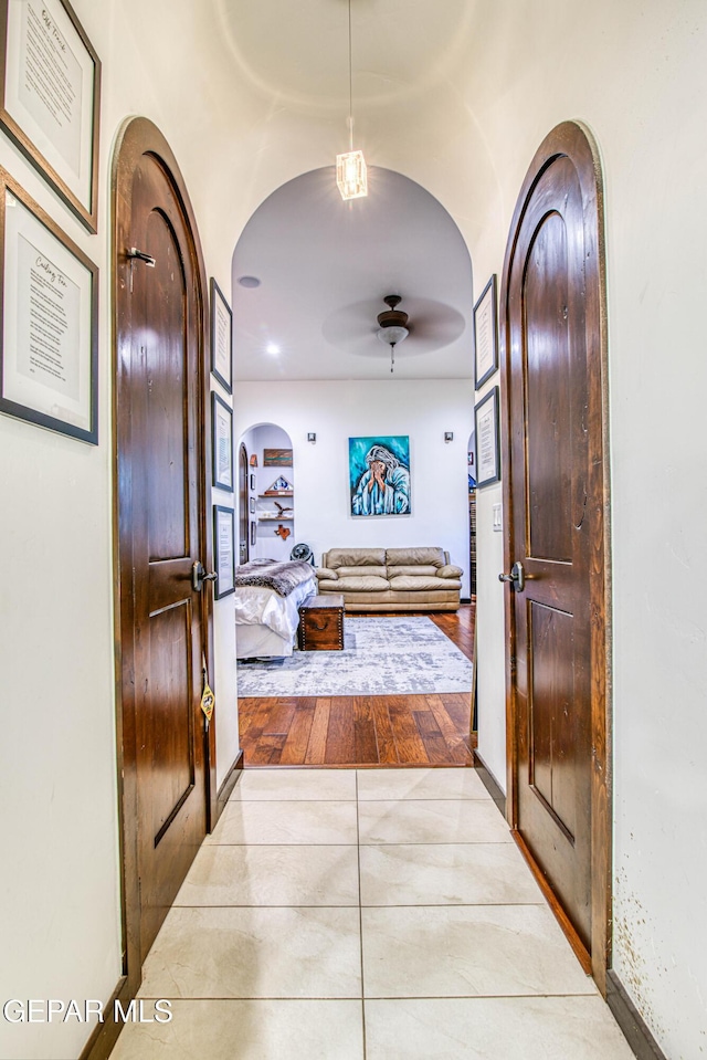 hall featuring arched walkways, tile patterned floors, and baseboards