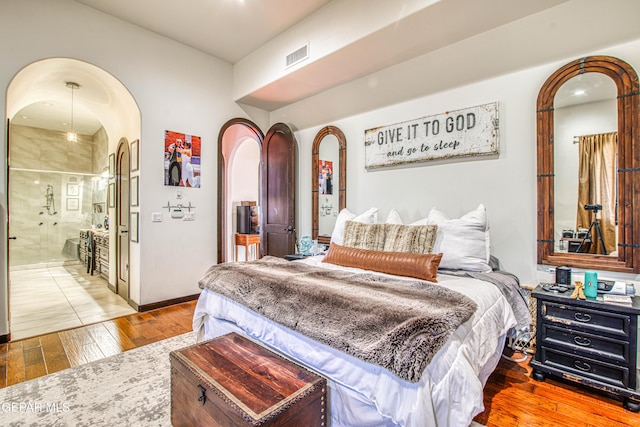 bedroom with arched walkways and hardwood / wood-style floors