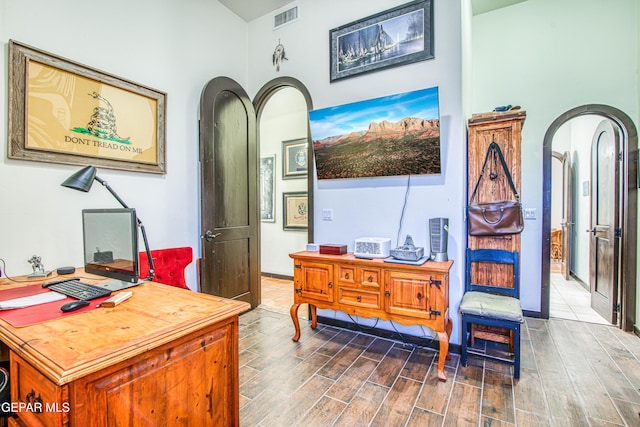 home office with arched walkways, wood finished floors, and a high ceiling
