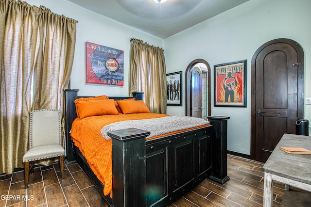 bedroom featuring wood tiled floors, arched walkways, and baseboards