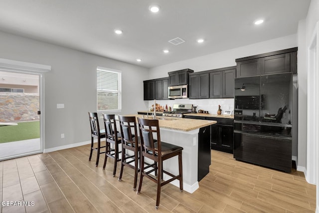 13868 Sky Ranger Ave, El Paso, TX 79928 - kitchen featuring stainless steel appliances, dark cabinets, an island with sink, light wood finished floors, and recessed lighting
