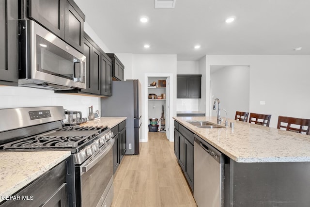 13868 Sky Ranger Ave, El Paso, TX 79928 - kitchen featuring appliances with stainless steel finishes, a sink, a center island with sink, light wood-style flooring, and light stone countertops