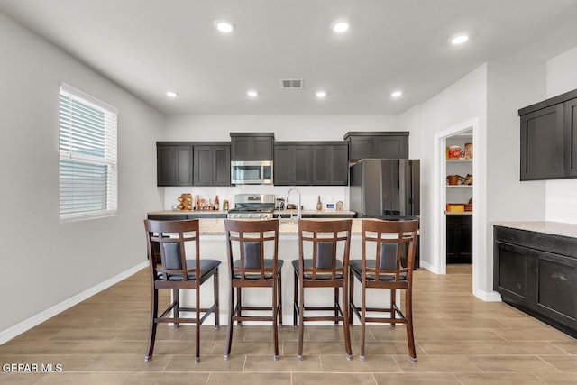 13868 Sky Ranger Ave, El Paso, TX 79928 - kitchen featuring appliances with stainless steel finishes, a center island with sink, a breakfast bar area, recessed lighting, and light wood-type flooring