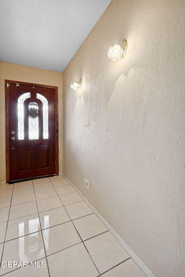 entryway featuring baseboards, light tile patterned floors, a textured wall, and a textured ceiling