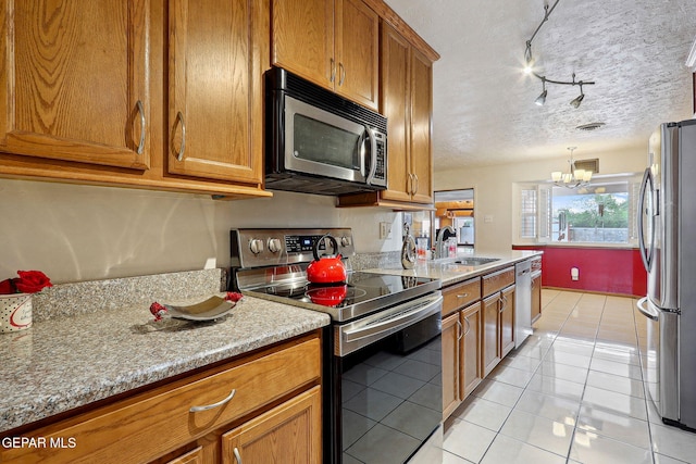 kitchen featuring appliances with stainless steel finishes, brown cabinetry, light tile patterned floors, a sink, and a chandelier