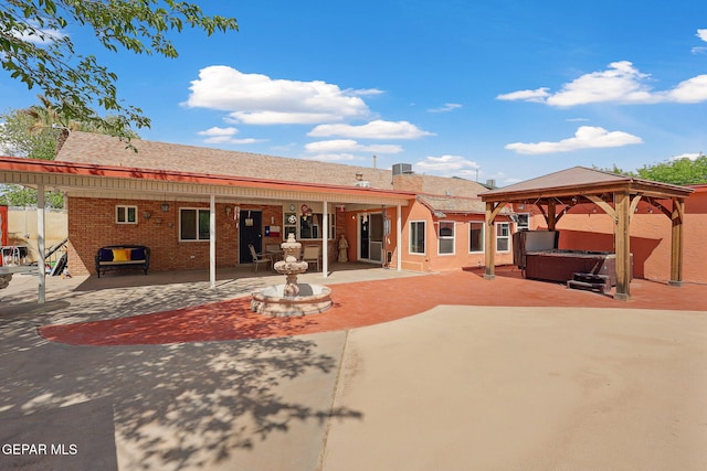 rear view of house featuring a hot tub, a patio area, brick siding, and a gazebo
