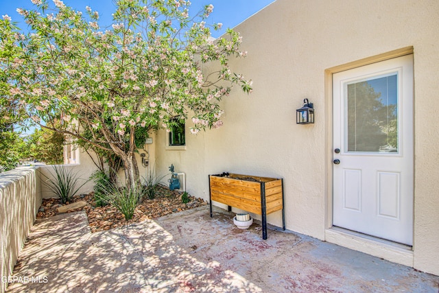 view of exterior entry featuring stucco siding, a patio, and fence