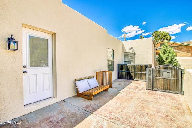 view of exterior entry featuring stucco siding, a gate, and a patio area
