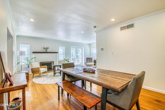 dining room with ornamental molding, a glass covered fireplace, plenty of natural light, light wood finished floors, and recessed lighting