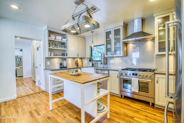 kitchen with appliances with stainless steel finishes, wall chimney range hood, open shelves, butcher block countertops, and a sink