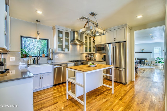 kitchen featuring stainless steel appliances, wall chimney exhaust hood, a sink, wooden counters, and backsplash