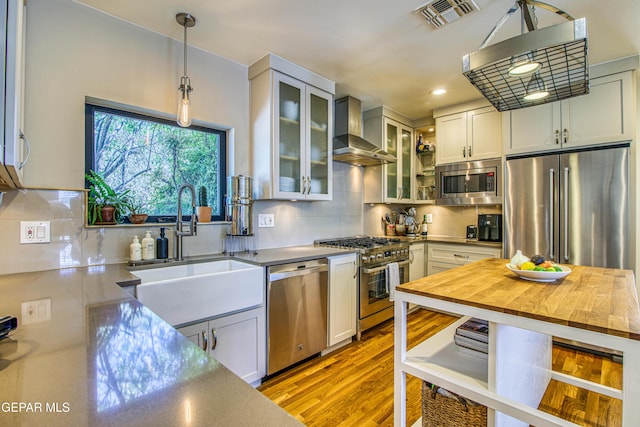 kitchen featuring premium appliances, wall chimney exhaust hood, a sink, tasteful backsplash, and recessed lighting