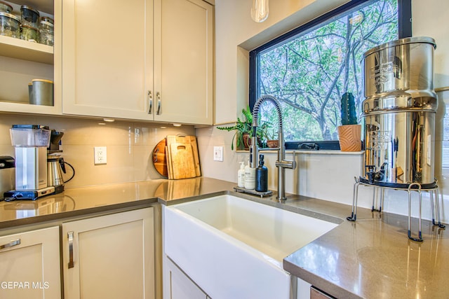 kitchen featuring a sink, tasteful backsplash, white cabinetry, and glass insert cabinets