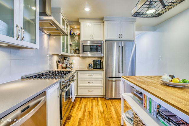 kitchen with stainless steel appliances, wall chimney exhaust hood, light wood finished floors, light countertops, and recessed lighting