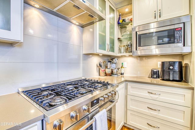 kitchen featuring appliances with stainless steel finishes, light countertops, custom range hood, and glass insert cabinets