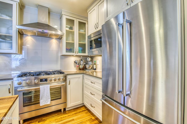 kitchen with stainless steel appliances, wall chimney exhaust hood, wooden counters, light wood-style flooring, and white cabinets