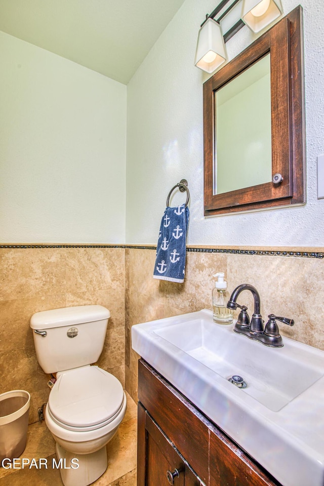 half bathroom featuring toilet, vanity, a wainscoted wall, and tile walls