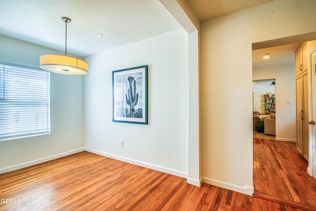 empty room with wood finished floors, a ceiling fan, and baseboards