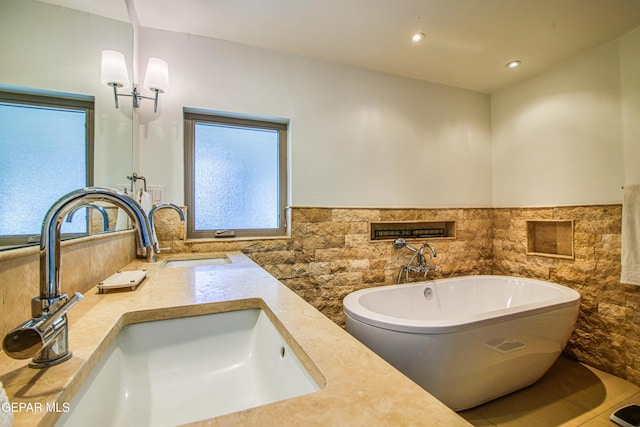 bathroom with a sink, a freestanding bath, wainscoting, tile walls, and a chandelier