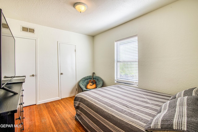 bedroom with hardwood / wood-style flooring, baseboards, a textured wall, and a textured ceiling