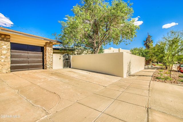 view of home's exterior featuring a gate, stone siding, driveway, a garage, and stucco siding