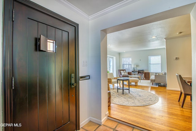 foyer with ornamental molding, baseboards, and light wood-style flooring