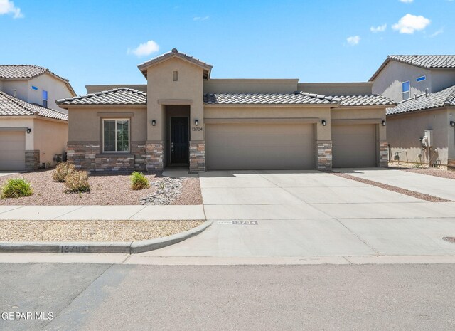 mediterranean / spanish-style home featuring an attached garage, stucco siding, stone siding, and driveway