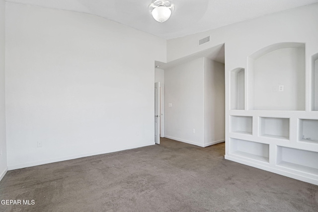 empty room featuring lofted ceiling, carpet, baseboards, and visible vents