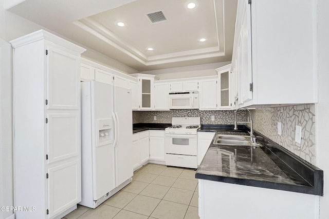 kitchen featuring light tile patterned floors, a sink, dark countertops, a raised ceiling, and white appliances