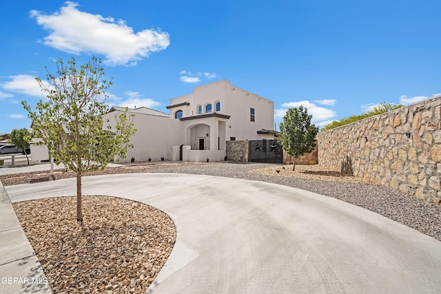 view of front facade featuring stucco siding, fence, and curved driveway