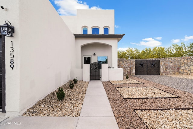 view of exterior entry with a gate, stucco siding, and fence