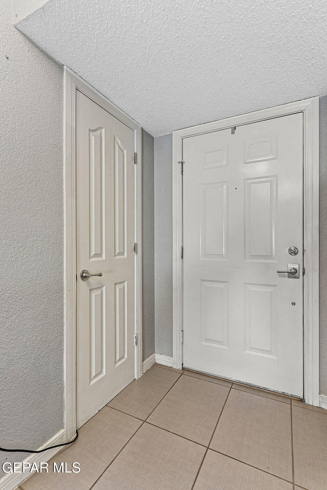 entryway featuring a textured ceiling, light tile patterned flooring, and a textured wall