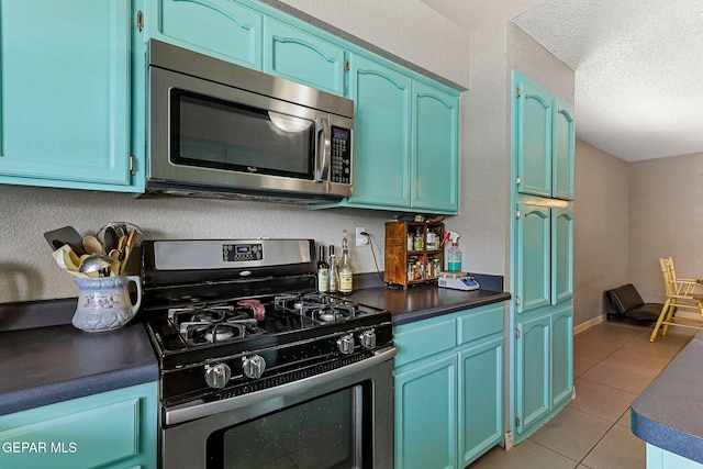 kitchen with appliances with stainless steel finishes, dark countertops, light tile patterned floors, blue cabinets, and a textured ceiling