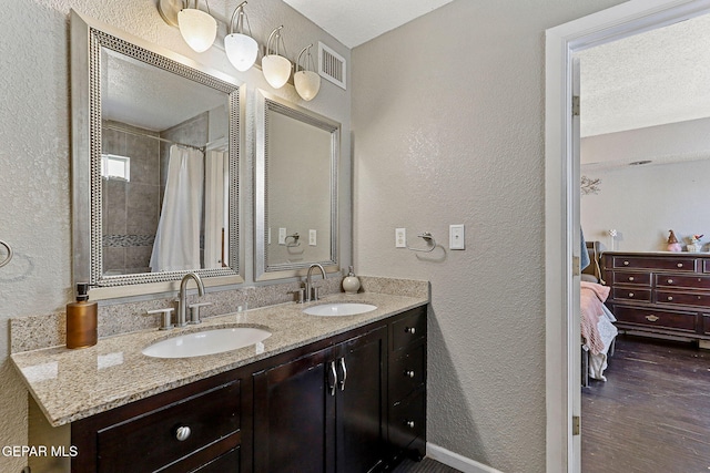 ensuite bathroom with connected bathroom, visible vents, a sink, and a textured wall