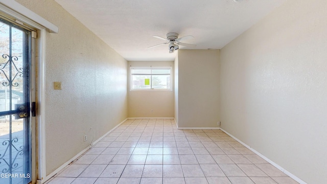 empty room with ceiling fan, a textured wall, light tile patterned flooring, and baseboards