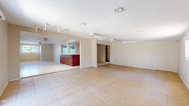 unfurnished living room with a ceiling fan, light tile patterned floors, baseboards, and a textured ceiling