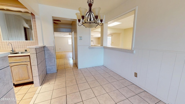 unfurnished dining area with a sink, light tile patterned flooring, a chandelier, wainscoting, and a ceiling fan