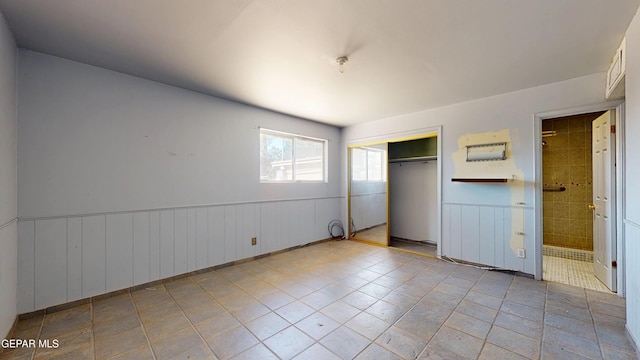 unfurnished bedroom featuring a wainscoted wall, a closet, tile patterned flooring, and connected bathroom