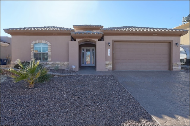 mediterranean / spanish-style house with stucco siding, concrete driveway, a tiled roof, stone siding, and an attached garage