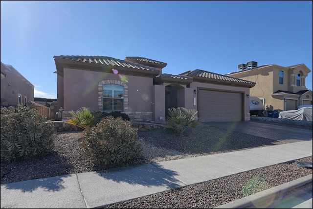 mediterranean / spanish-style home with a tile roof, stucco siding, concrete driveway, an attached garage, and central AC